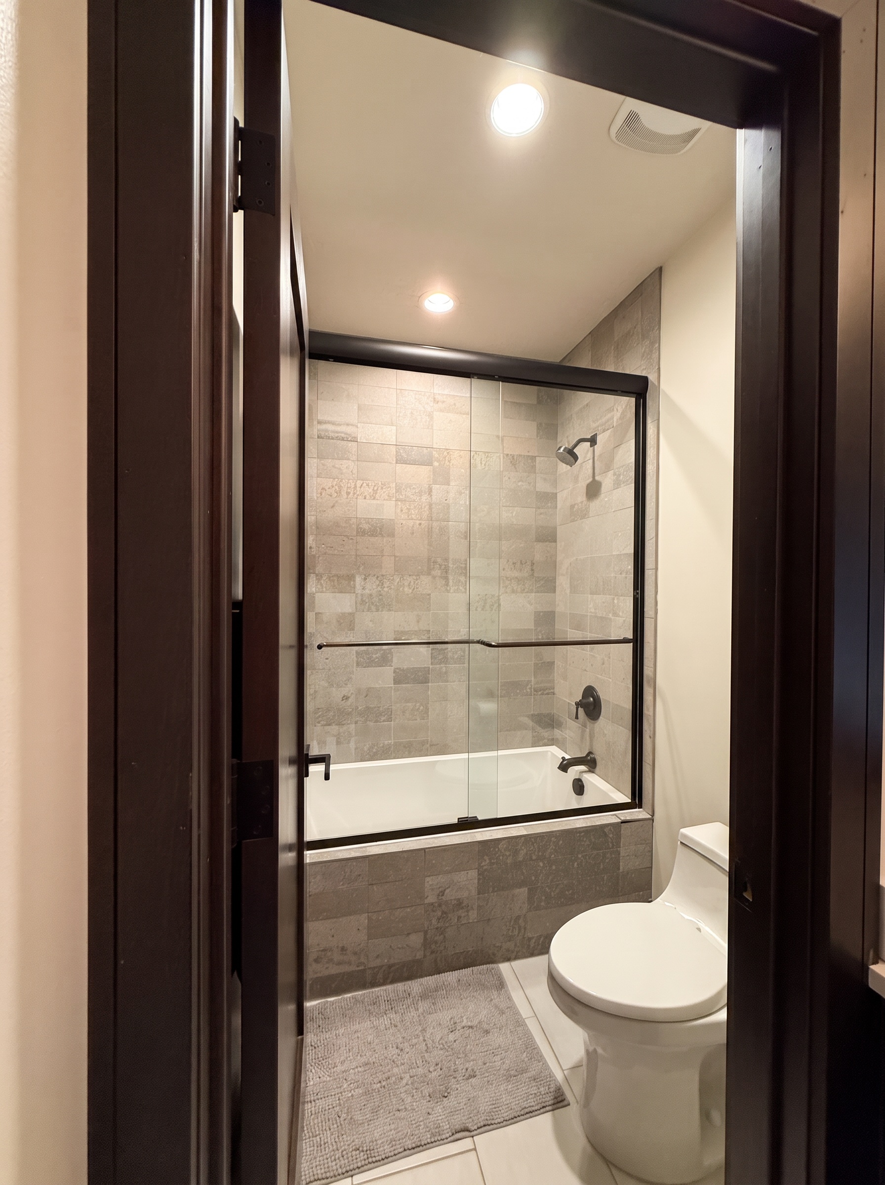 Glass shower over a deep tub with neutral stone tile and matte black hardware