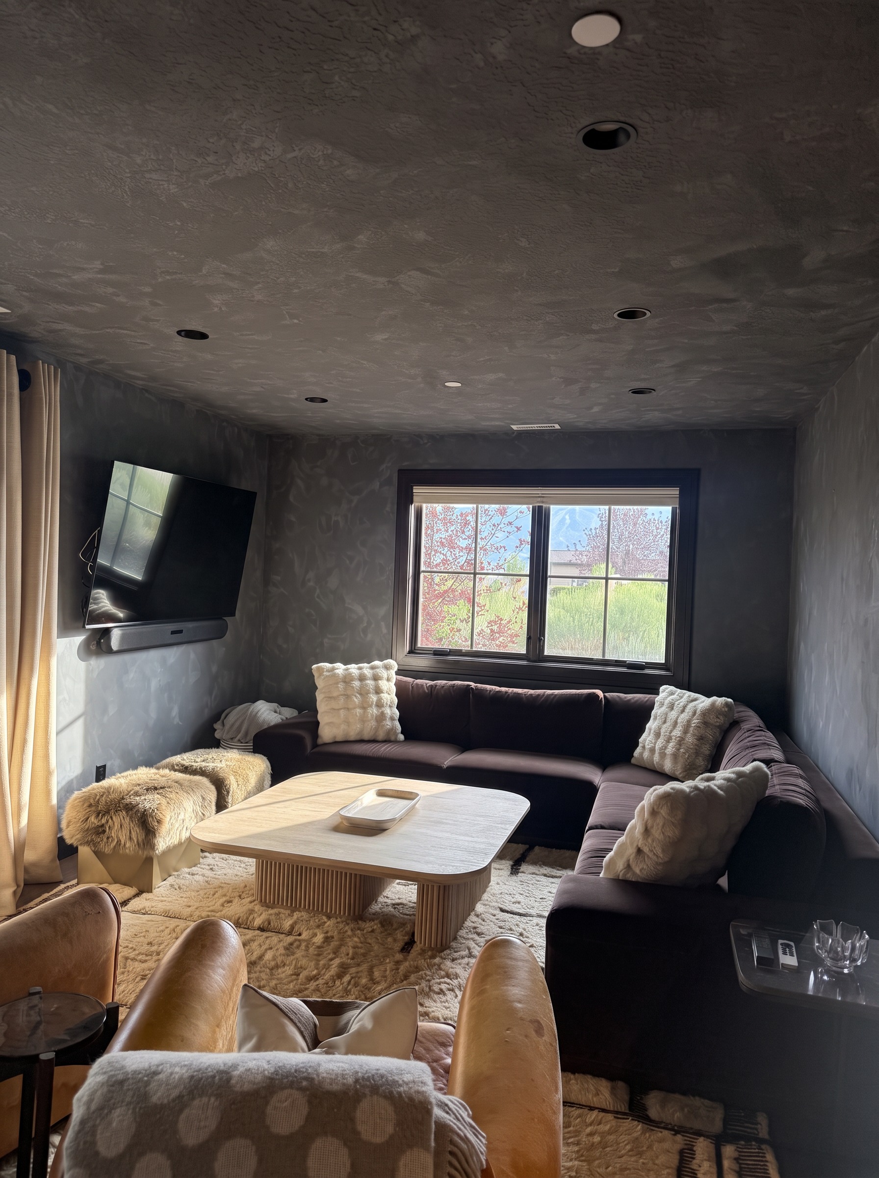 Lower level living room with a deep sectional, dark plaster walls, and a mountain-view window
