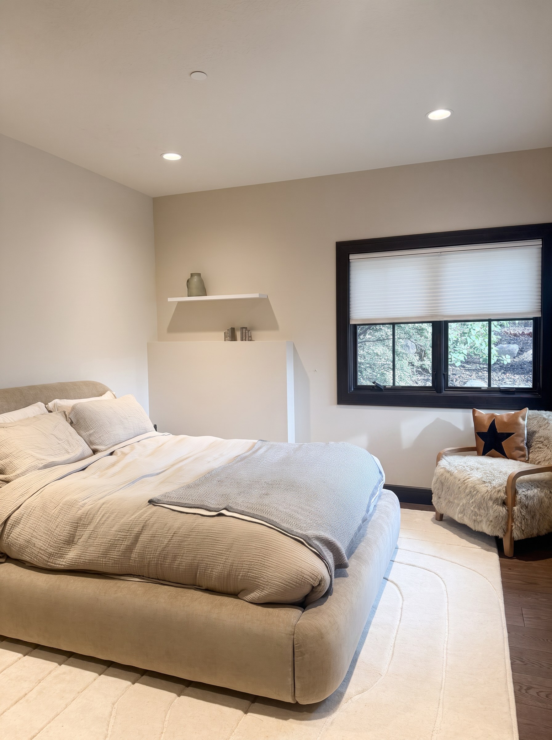 Queen bedroom with a low upholstered platform bed, floating shelf, and black-framed window