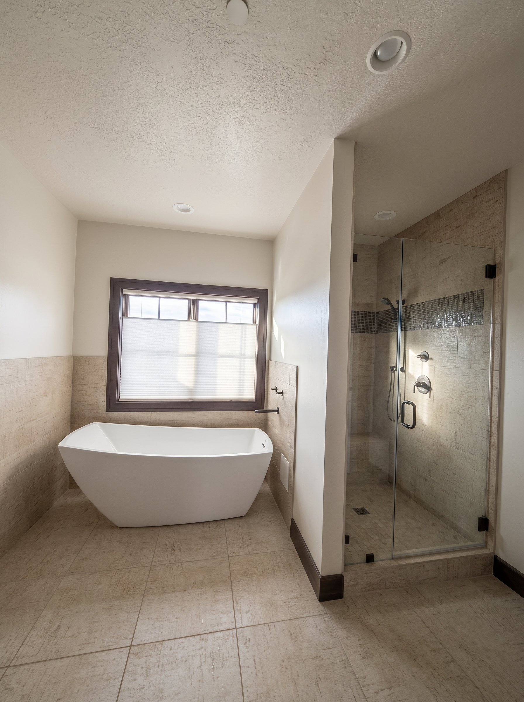 Freestanding soaking tub beneath a window beside a glass walk-in shower with stone tile