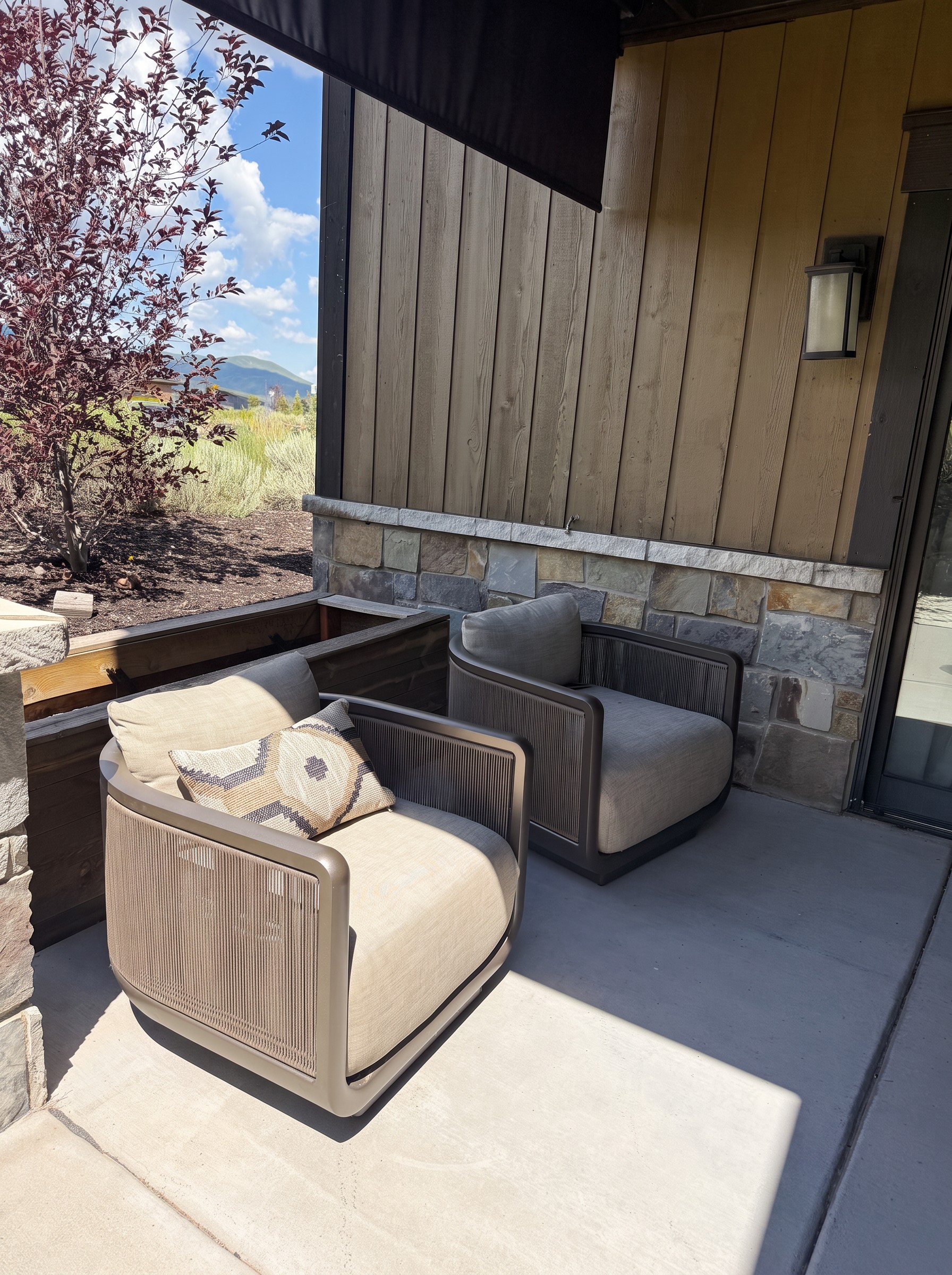 Two woven outdoor swivel chairs on the lower patio with a meadow and mountain view