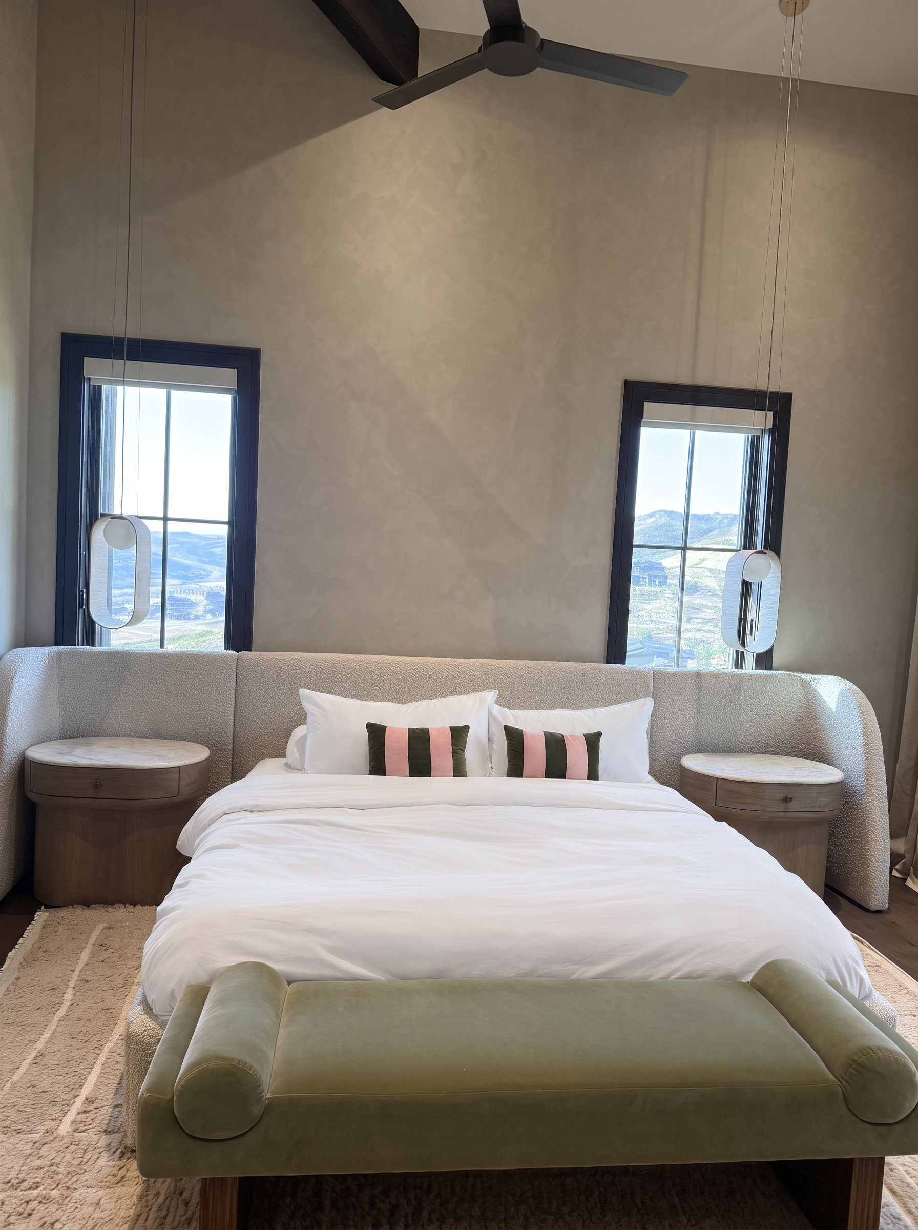 Primary suite with an upholstered bed, mountain-view windows, and a sculptural bench