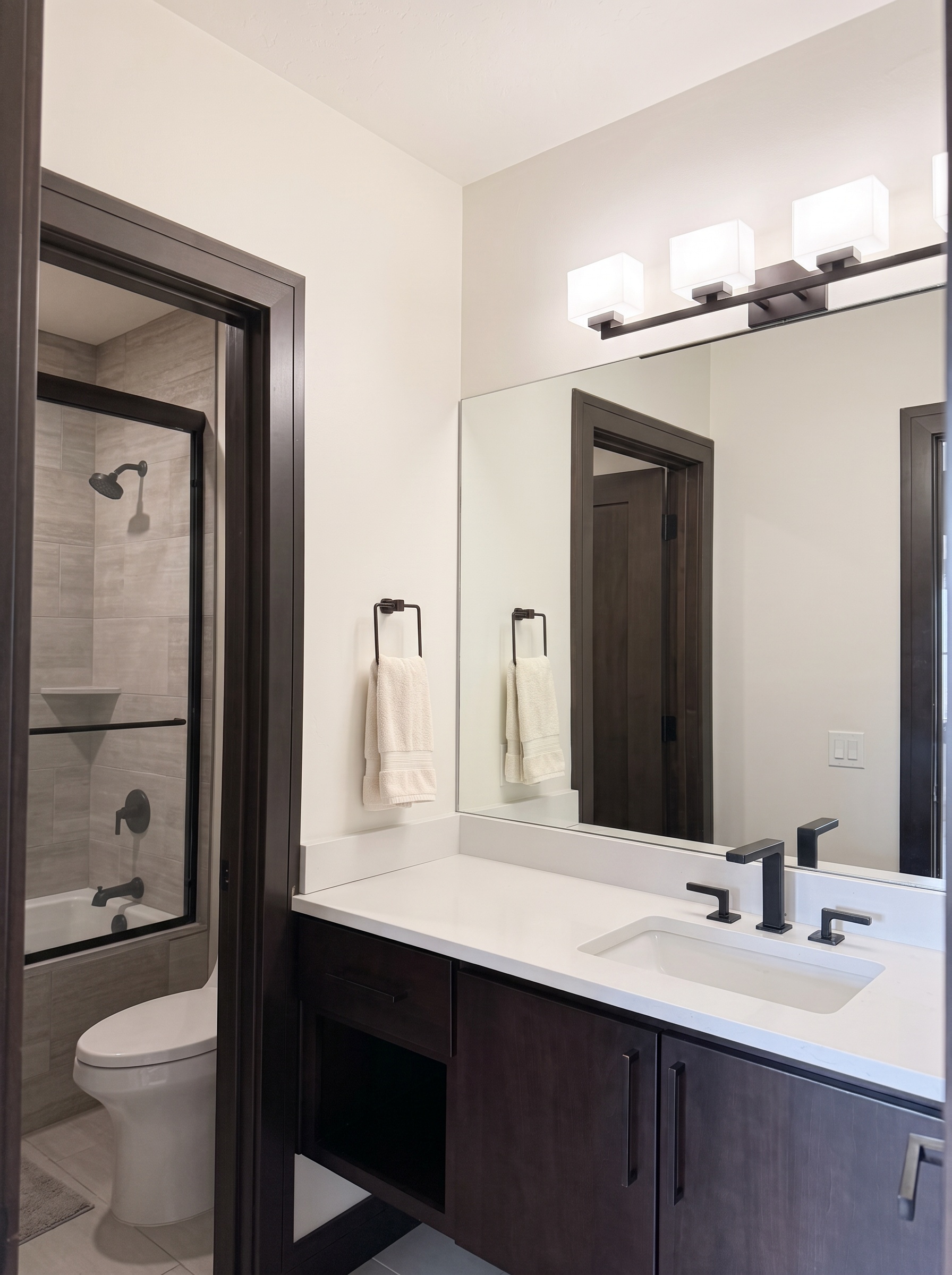 Lower en suite bath with espresso cabinets, light quartz vanity, and matte black fixtures