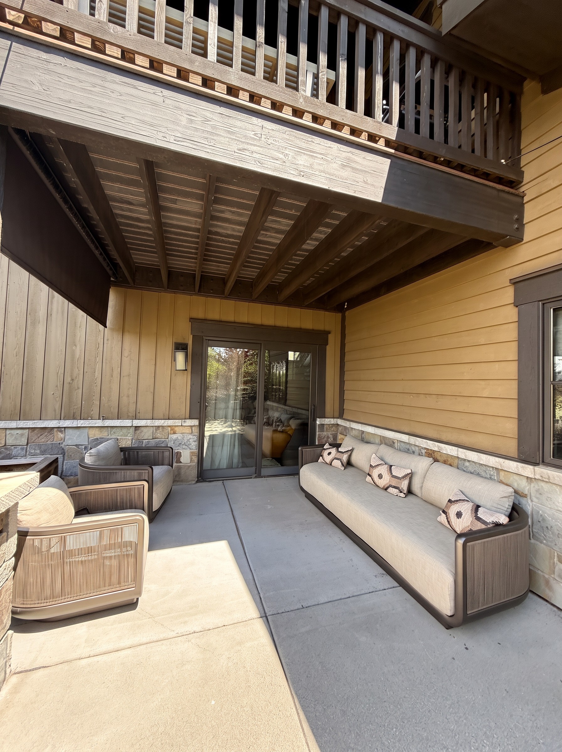 Covered lower patio with a long outdoor sofa, lounge chairs, and stone and timber walls