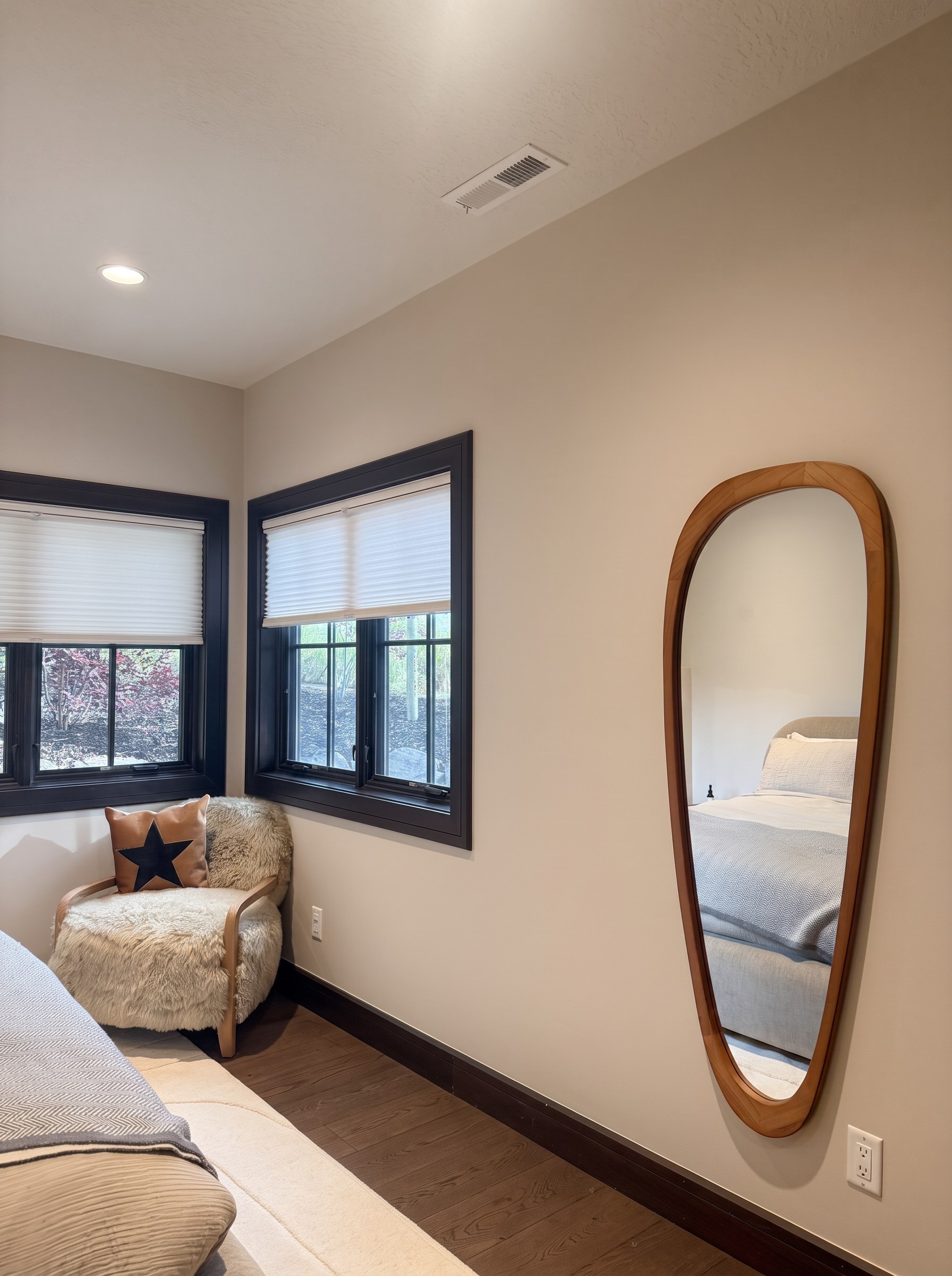 Corner windows with a sheepskin lounge chair and a sculptural oak floor mirror